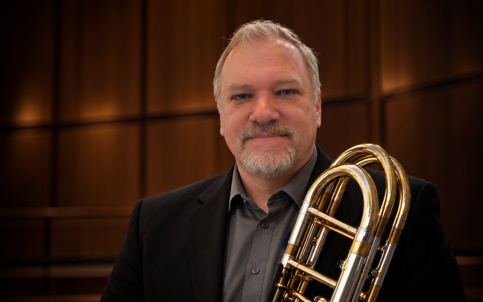 Dominick Walenczak in a wood-paneled concert hall, holding a bass trombone